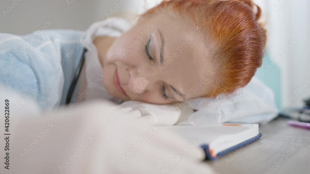 Close-up of exhausted overwhelmed doctor sleeping on table in hospital. Portrait of beautiful redhead Caucasian woman tired working on coronavirus pandemic outbreak. Overworking concept. Close-up of exhausted overwhelmed doctor sleeping on table in hospital. Portrait of beautiful redhead Caucasian woman tired working on coronavirus pandemic outbreak. Overworking concept.