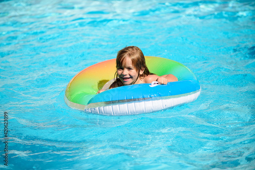 Kid in swimming pool, relax swim on inflatable ring and has fun in water on summer vacation. Healthy child lifestyle.