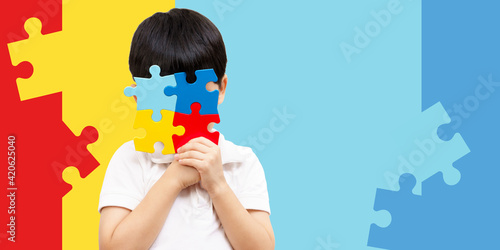 World autism awareness day April 2 - Studio Portrait of a cute asian boy cover his face with the colorful puzzles pieces. Autism Spectrum Disorder concept, ASD, Syndrome, Light it up blue, Backdrop.