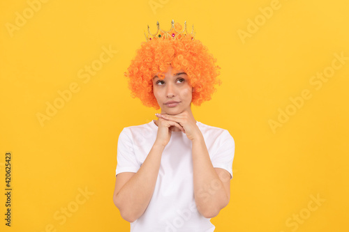 egoistic funny girl with fancy look wearing orange hair wig and princess crown, imagining
