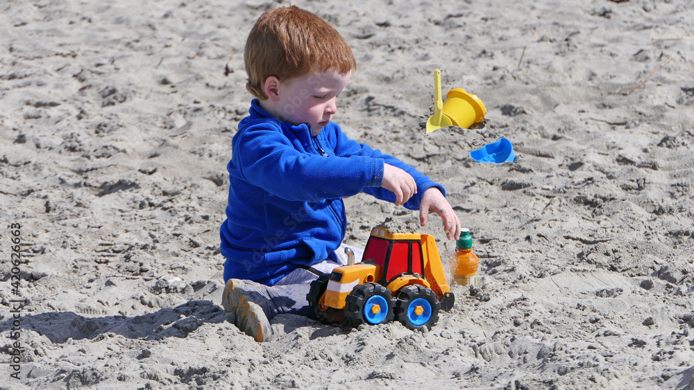 Red headed boy playing with Bucket spade and Digger on a sandy beach Red headed boy playing with Bucket spade and Digger on a sandy beach