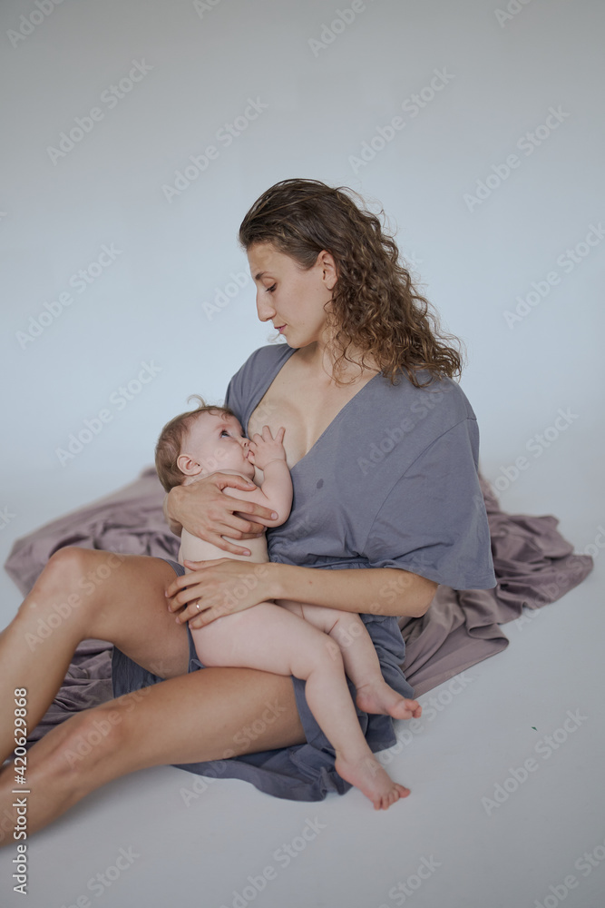 a young mother with a baby girl, curly hair woman breastfeeding and hugging her daughter a young mother with a baby girl, curly hair woman breastfeeding and hugging her daughter