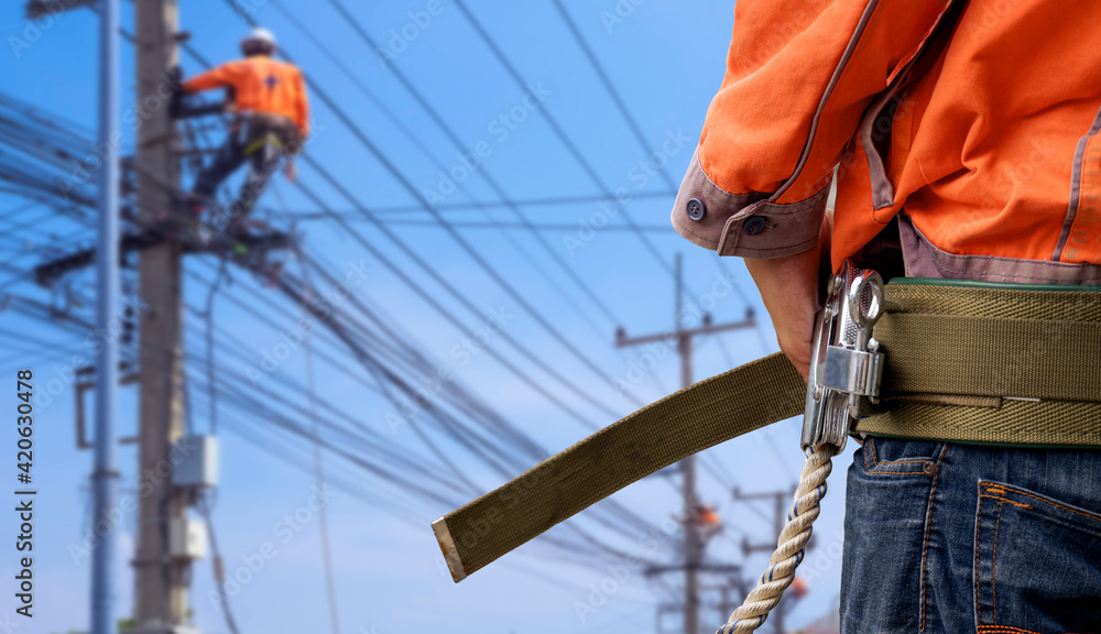 Midsection of electrician lineman wearing safety belt with blurred background of electrical workers team are working on power poles in public area