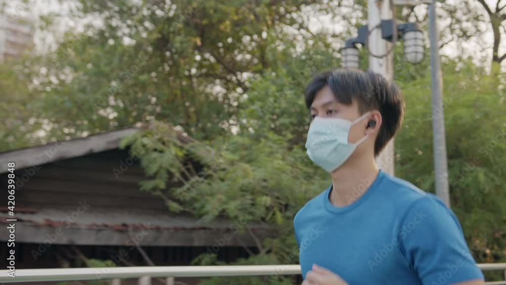 Asian man is exercising wearing a protection mask epidemic of flu or covid-19 while running on the bridge in the city. Concept healthy running and outdoor exercise Asian man is exercising wearing a protection mask epidemic of flu or covid-19 while running on the bridge in the city. Concept healthy running and outdoor exercise