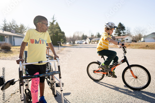 Boy with leg in pink cast watches brother ride bike photo