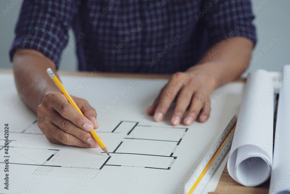 Architect or engineer hands working on blueprint plans with a pencil ,laptop a ruler, calculator, and engineering tools. Architect or engineer working on blueprint in office. Architect or engineer hands working on blueprint plans with a pencil ,laptop a ruler, calculator, and engineering tools. Architect or engineer working on blueprint in office.