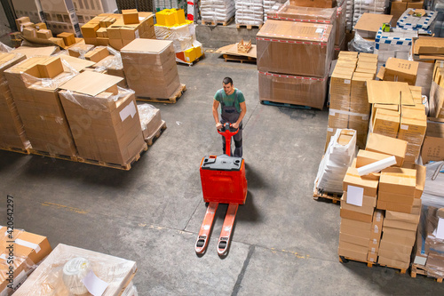 One man operates the pallet jack in a warehouse full of shipping goods photo