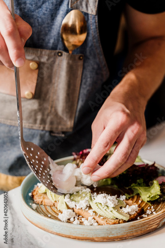 Hands of cook placing poached eggs on top of avocado toast in a nice plate in kitchen restaurant