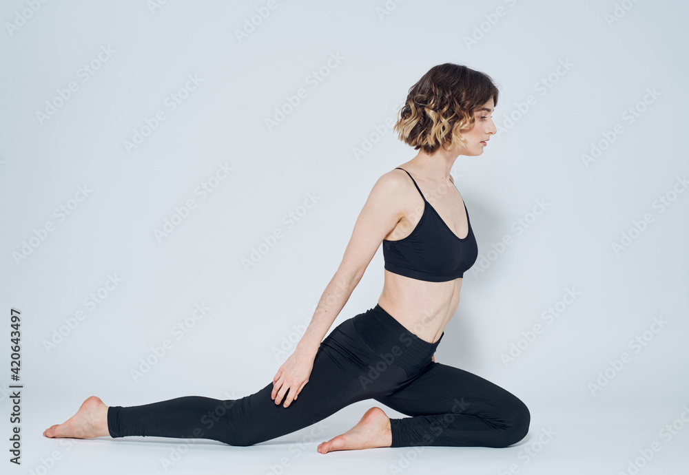 A woman in black jeans sits on the floor on one leg and gestures with her hands