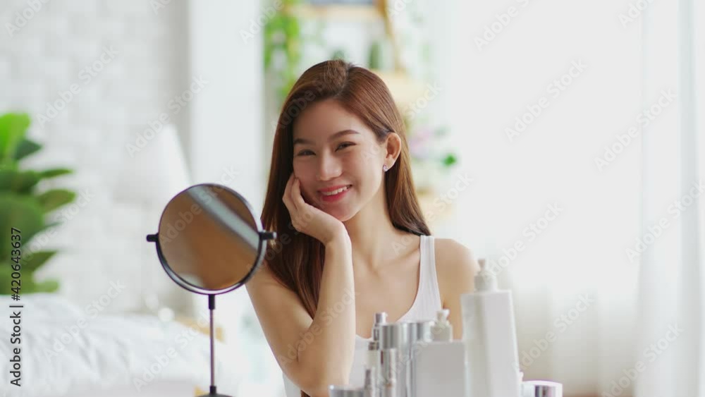 Happy Asian young woman smile and looking in mirror doing skin care touch cheek and beauty treatment at home,Wellness woman self care with beauty product at home Happy Asian young woman smile and looking in mirror doing skin care touch cheek and beauty treatment at home,Wellness woman self care with beauty product at home