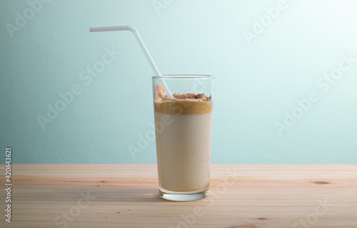 Trendy Korean beverage Dalgona coffee and a straw in a glass on a tabletop, close up side view. made with instant coffee and fresh milk with added sugar and chocolate crumbs on top.