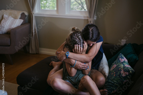 Two sisters hugging and making up after having a disagreement at home.
