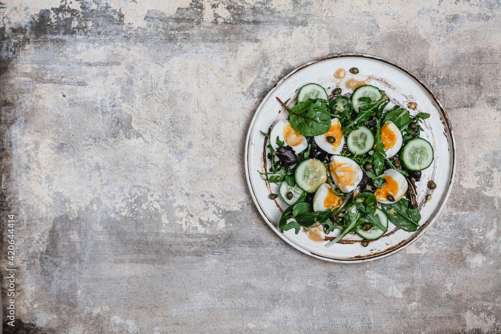 salad with fresh cucumbers, herbs, soft boiled eggs and lemon dressing on ceramic plate, seasonal healthy eating concept, copy space