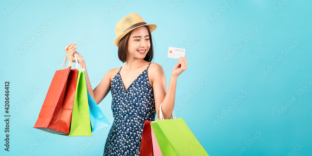 Young Asian woman standing on a blue background and hand holding shopping bags with credit card. Young Asian woman standing on a blue background and hand holding shopping bags with credit card.