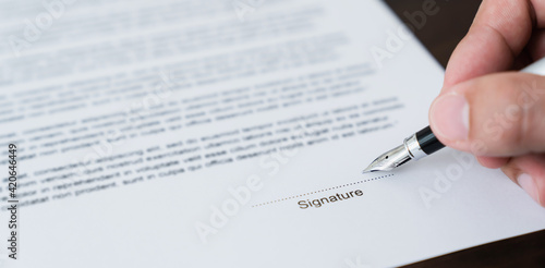 Hand holds pen and signs agreement contract on the table.