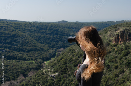 A young girl with long hair looks through binoculars at the scenery © Uri