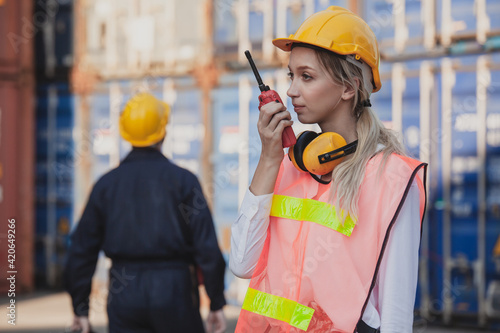 Female worker using handheld radio receiver for communication. working engineer in the construction container yard. Container Shipping Logistics Engineering concept