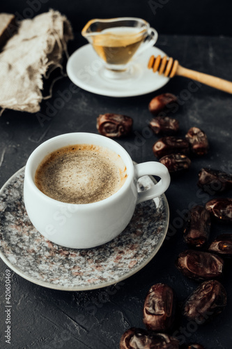 freshly brewed coffee with foam, dried dates on vintage dishes oriental in dark atmosphere. oriental sweets, honey honey stick, grain burlap cloth. oriental holiday layout, vertical, selective focus