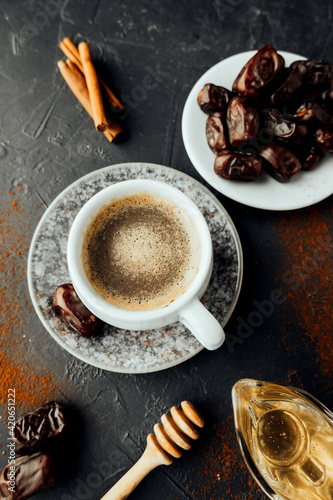 freshly brewed coffee with milk , dried dates, cinnamon sticks, honey, spilled coffee and spices, burlap cloth on dark background. colorful image national food and drink. top view, selective focus