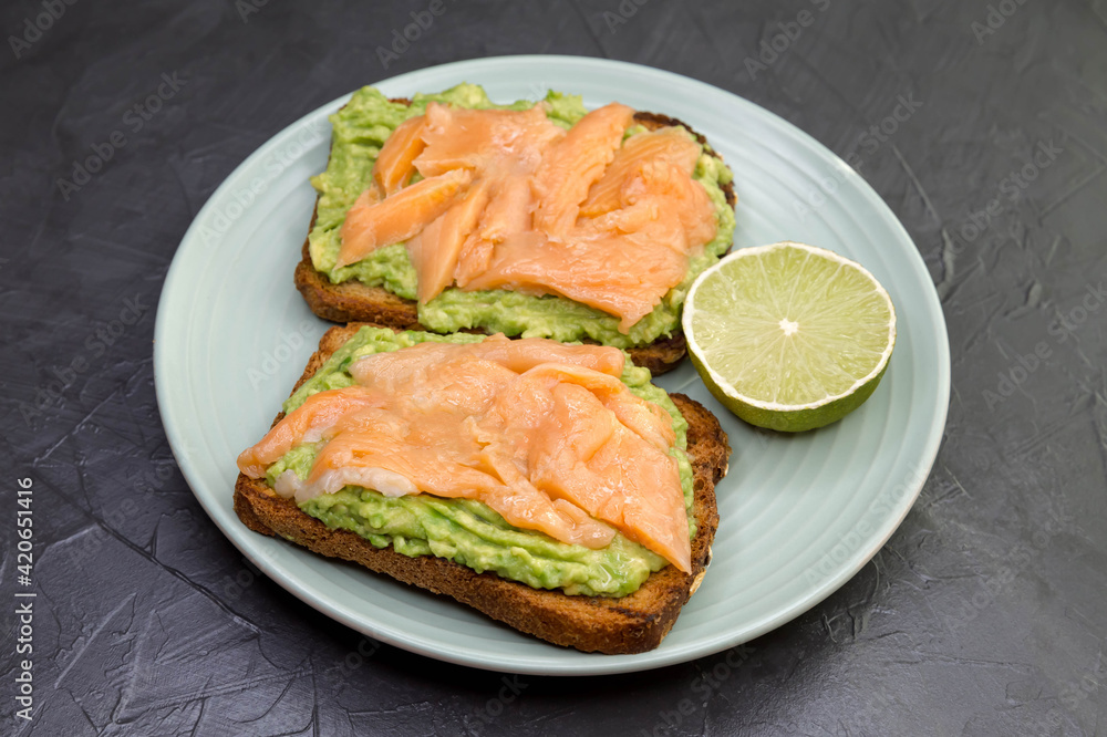 Closeup of toast with dark rye bread, guacamole, smoked salmon. Delicious sandwiches with avocado and salmon. Marble background with copy space. Healthy protein food, gourmet, breakfast, lunch concept