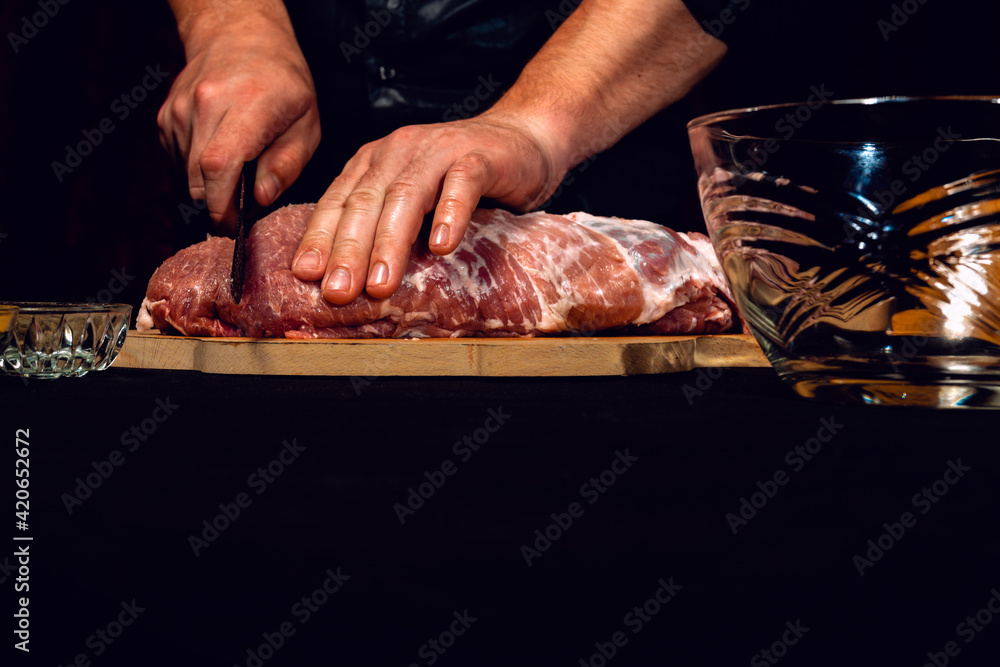 A large piece of raw pork, the cook cuts the pork neck in half.