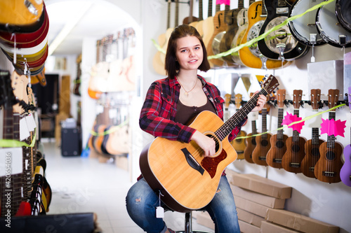 Customer girl is deciding on acoustic guitar in guitar shop.