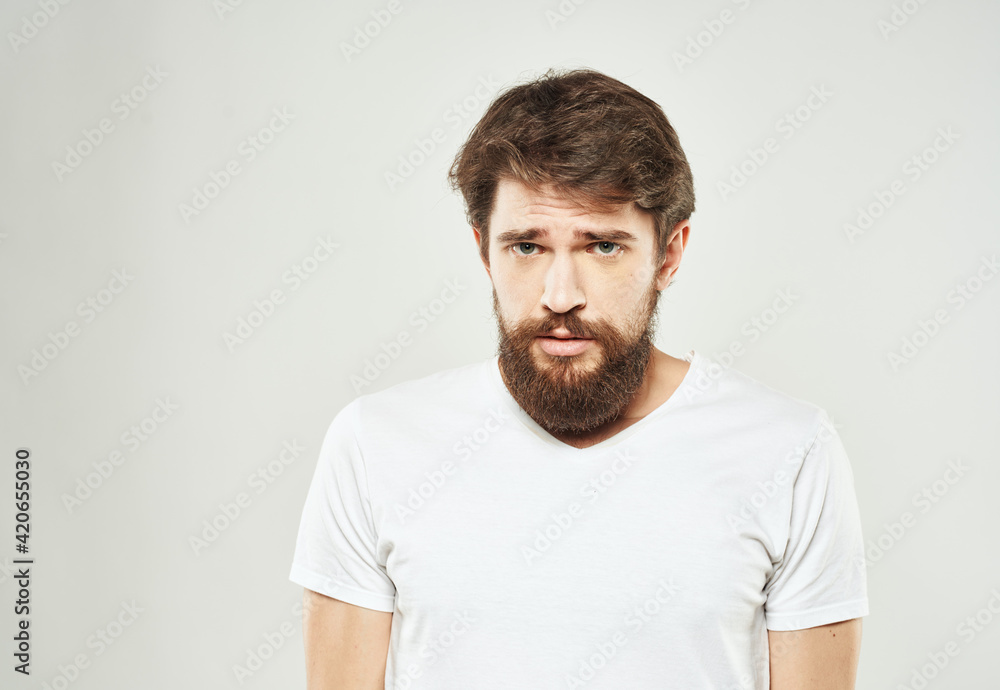 Emotional guy in a white T-shirt on a light background cropped view of a thick beard of a brunette Emotional guy in a white T-shirt on a light background cropped view of a thick beard of a brunette