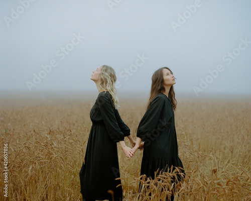 two girls in a black dress posing in a field among wheat ears