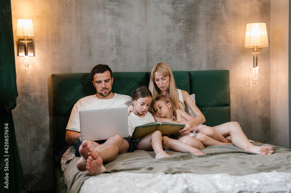 Mother reading book to daughters near working father Mother reading book to daughters near working father