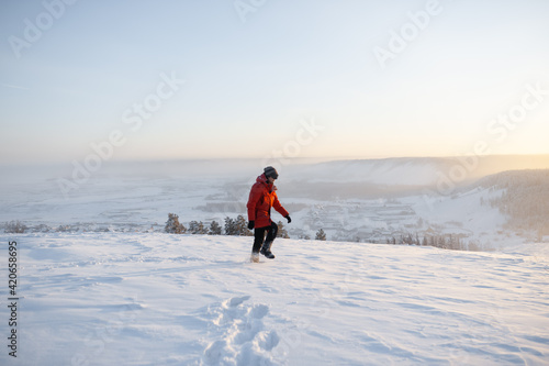 A man in a red jacket walks in the snow in winter