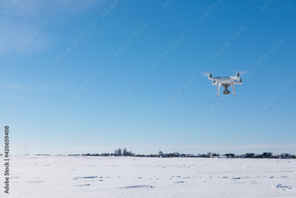 Drone flying above field covered with snow on sunny winter day