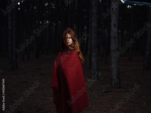Beautiful woman with a red cape in the black forest at night