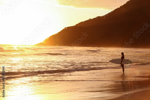 Beautiful surfer woman with surfboard in Brazilian beach at sunset