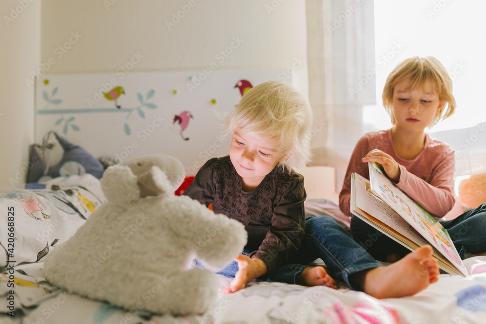 Little siblings with book sitting on bed Little siblings with book sitting on bed