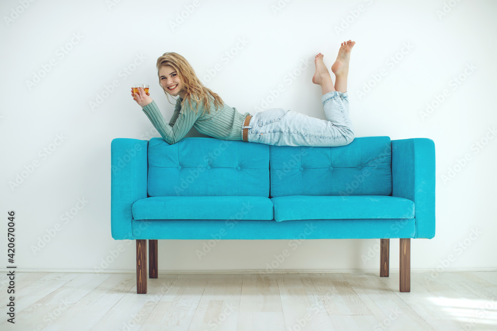 Beautiful woman is drinking tea on the sofa at home. Sportive young girl doing yoga pose on the couch. High quality photo. Beautiful woman is drinking tea on the sofa at home. Sportive young girl doing yoga pose on the couch. High quality photo.