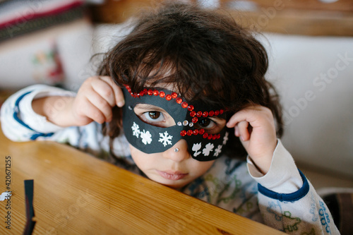 Kid covering her face with a decorated cardboard mask looking at camera photo