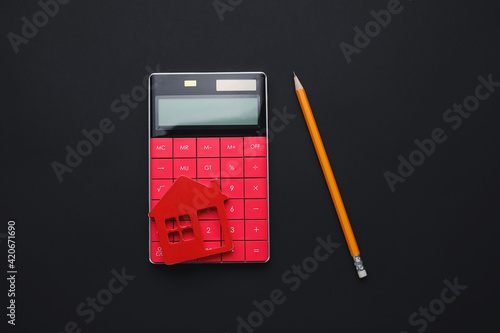 Calculator with model of house and pencil on dark background