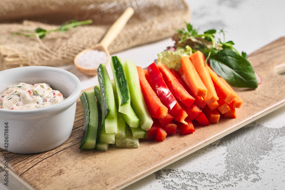 Fresh vegetable food platter on white table. Slices vegetable on wooden board with dip sauce. Rustic food concept.