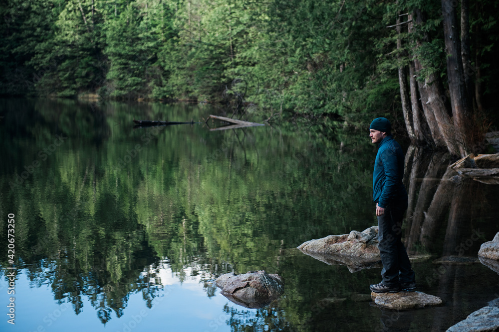 Man in blue jacket admires the calm surface of a lake. Man in blue jacket admires the calm surface of a lake.