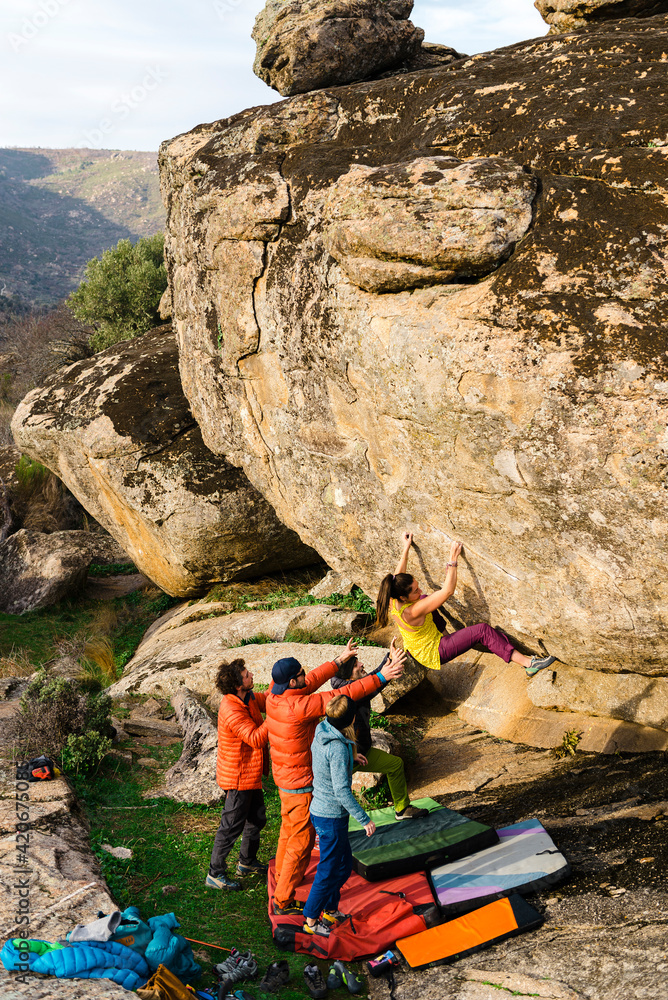 Woman climbing granite boulder rock near friends Woman climbing granite boulder rock near friends