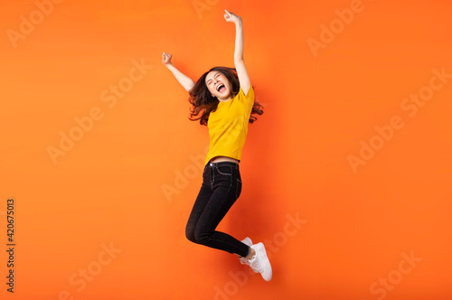 Young asian girl jumping up on orange background photo