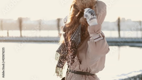 Winter girl portrait. Beauty joyful model girl blowing snow, having fun in winter park. Beautiful young woman enjoying nature outdoors. Wintertime.