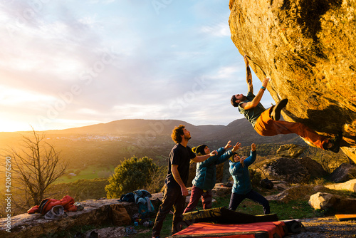 Man climbing granite boulder rock near friends photo