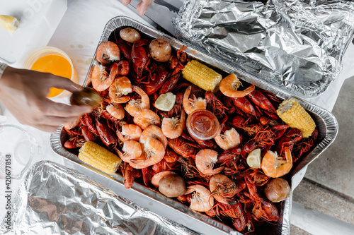 A hand reaching for Crawfish / Crayfish and boiled shrimp and corn