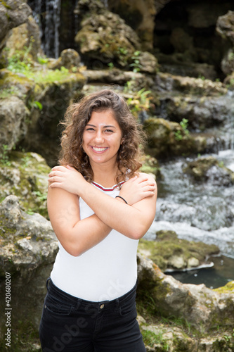 Happy beautiful young woman smiling broadly with arms on chest crossed smile brown long hair during walking lake coast park posing on nature background