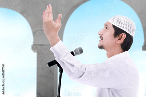 Asian Muslim man standing while raised hands and giving a sermon