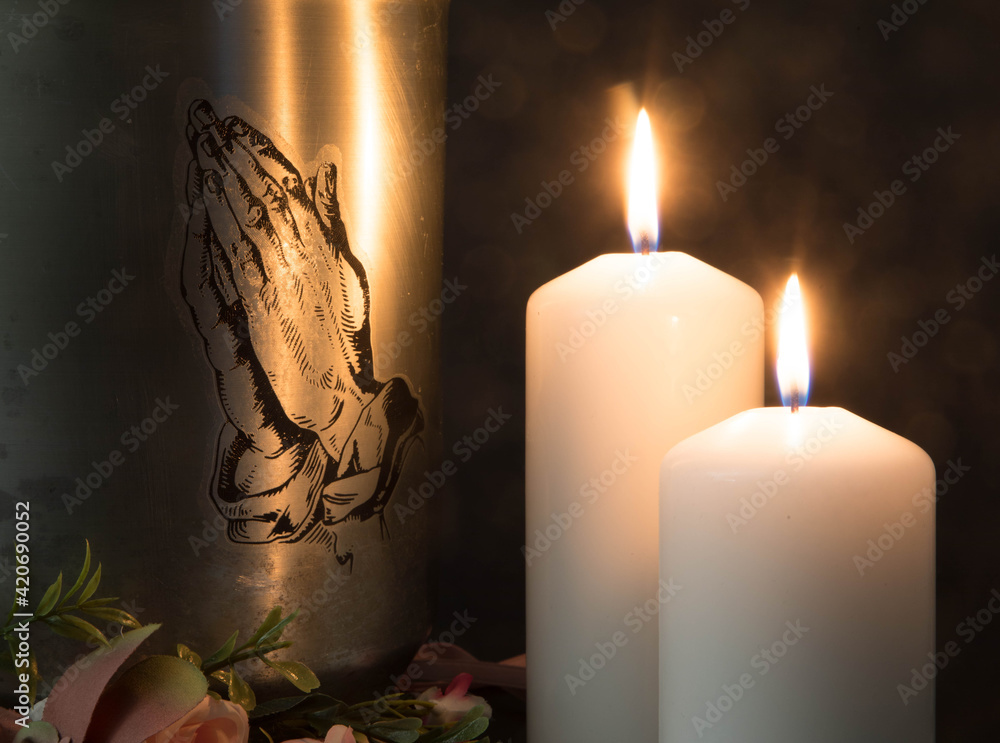 A metal urn with praying hands and burning candles with ashes from a dead  person at