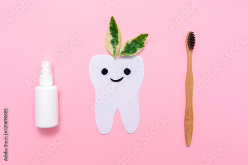 The concept of eco friendly hygiene products. A bamboo toothbrush, mouth freshener and cut out tooth of felt with green leafs. Pink background. Flat lay © _KUBE_