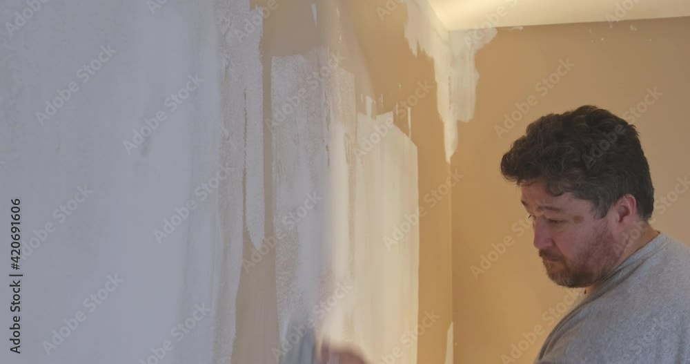 Worker smoothing and finishing wall with sanding the plaster