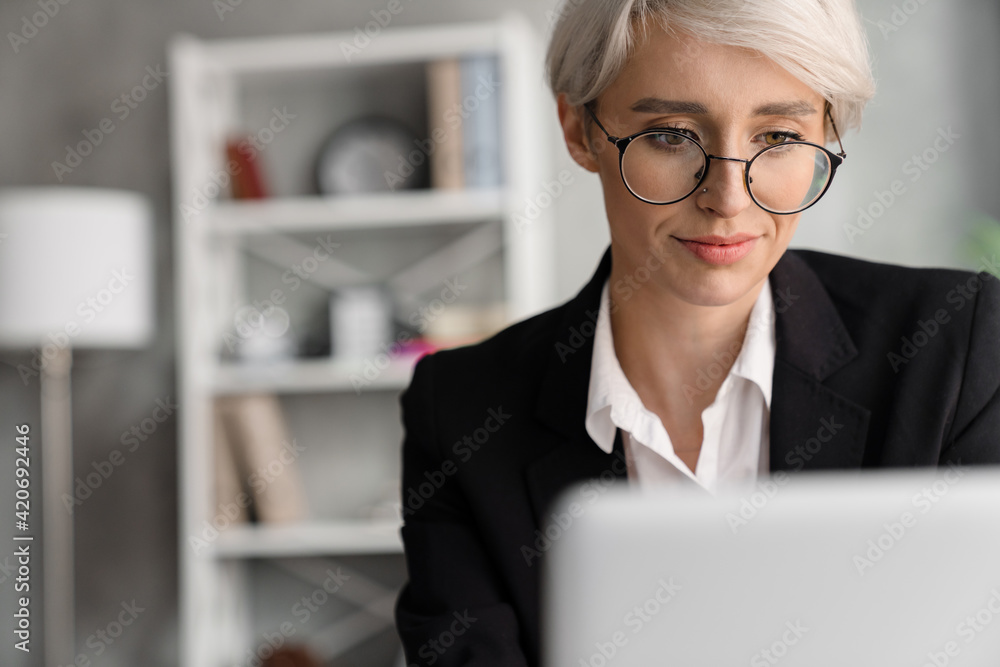 White-haired focused woman working with laptop while sitting at table White-haired focused woman working with laptop while sitting at table